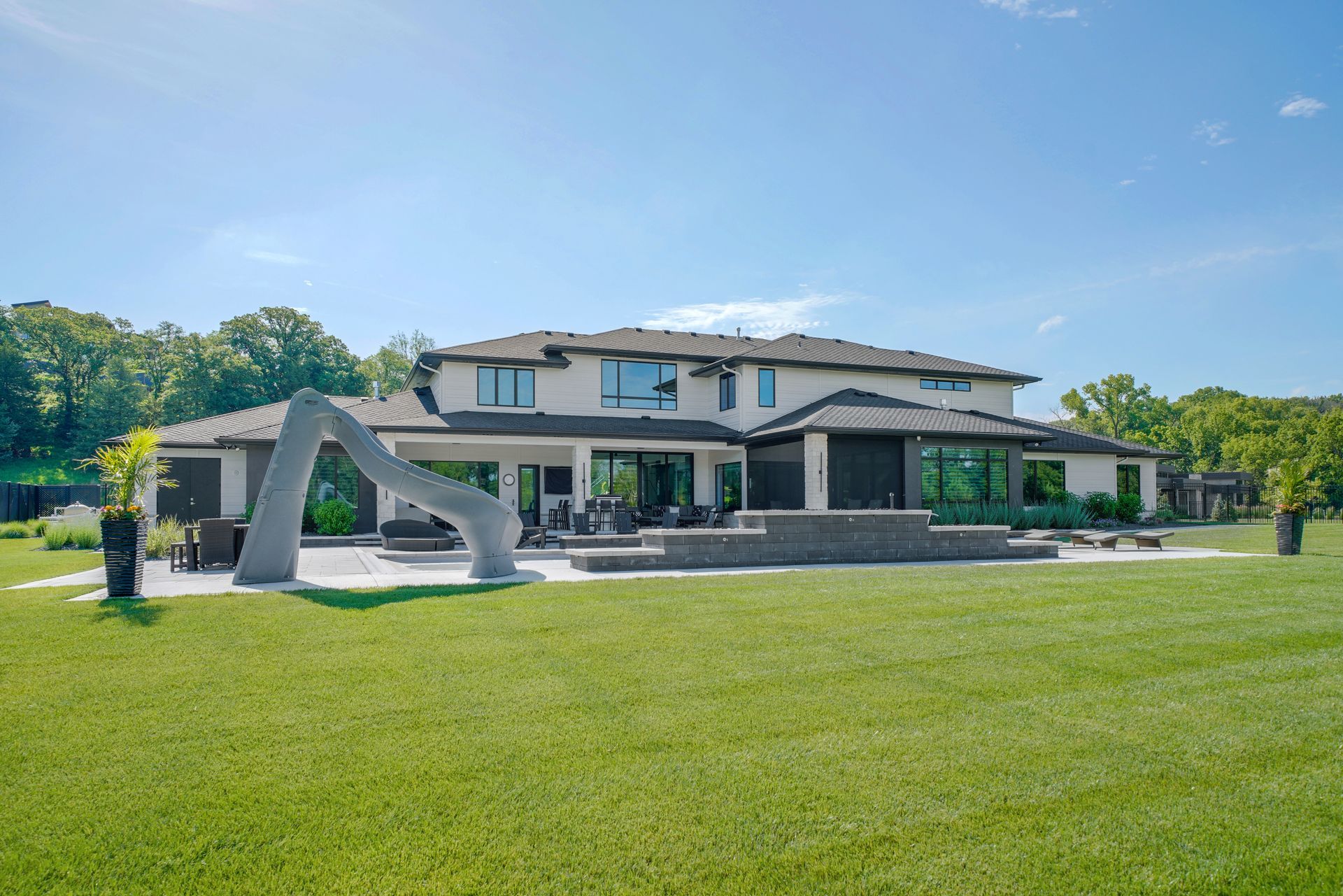 Large, modern house with a gray slide in the backyard on a sunny day.