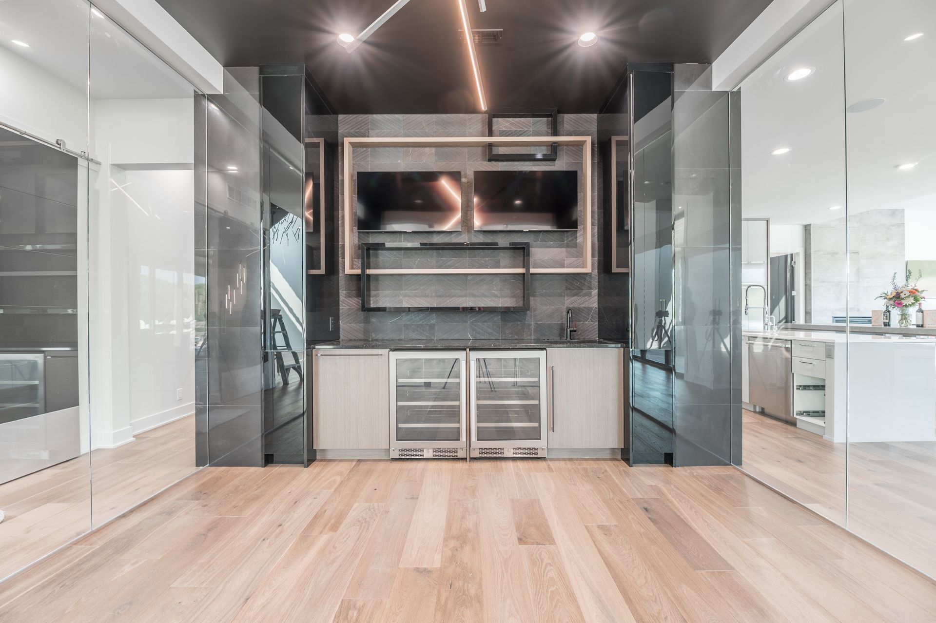 Modern home entertainment center with two TVs, two refrigerators, and wood floors.