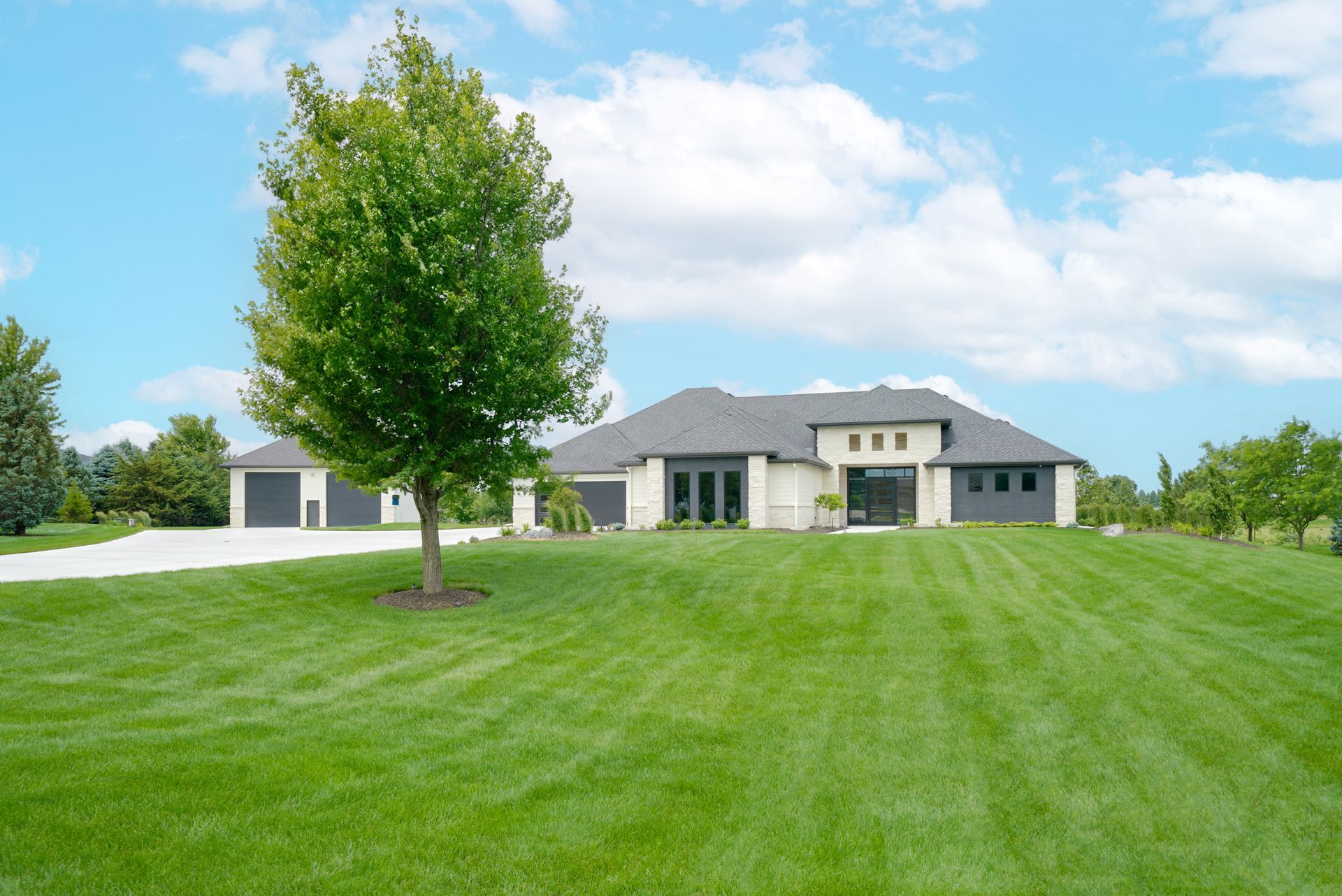 A large, modern house with a green lawn, tree, and a blue sky with clouds.