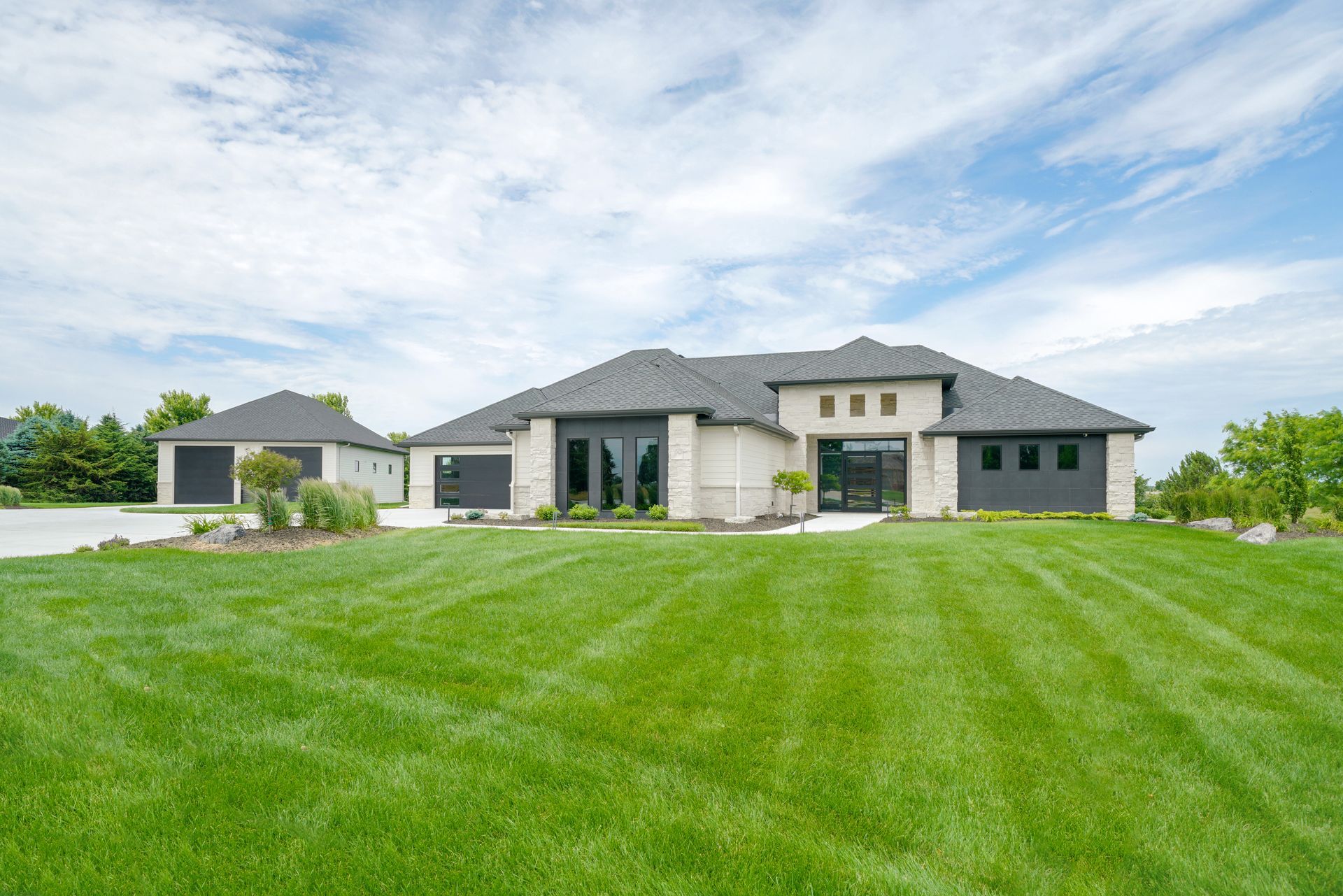 Modern, single-story house with attached garage, manicured lawn, and blue sky.