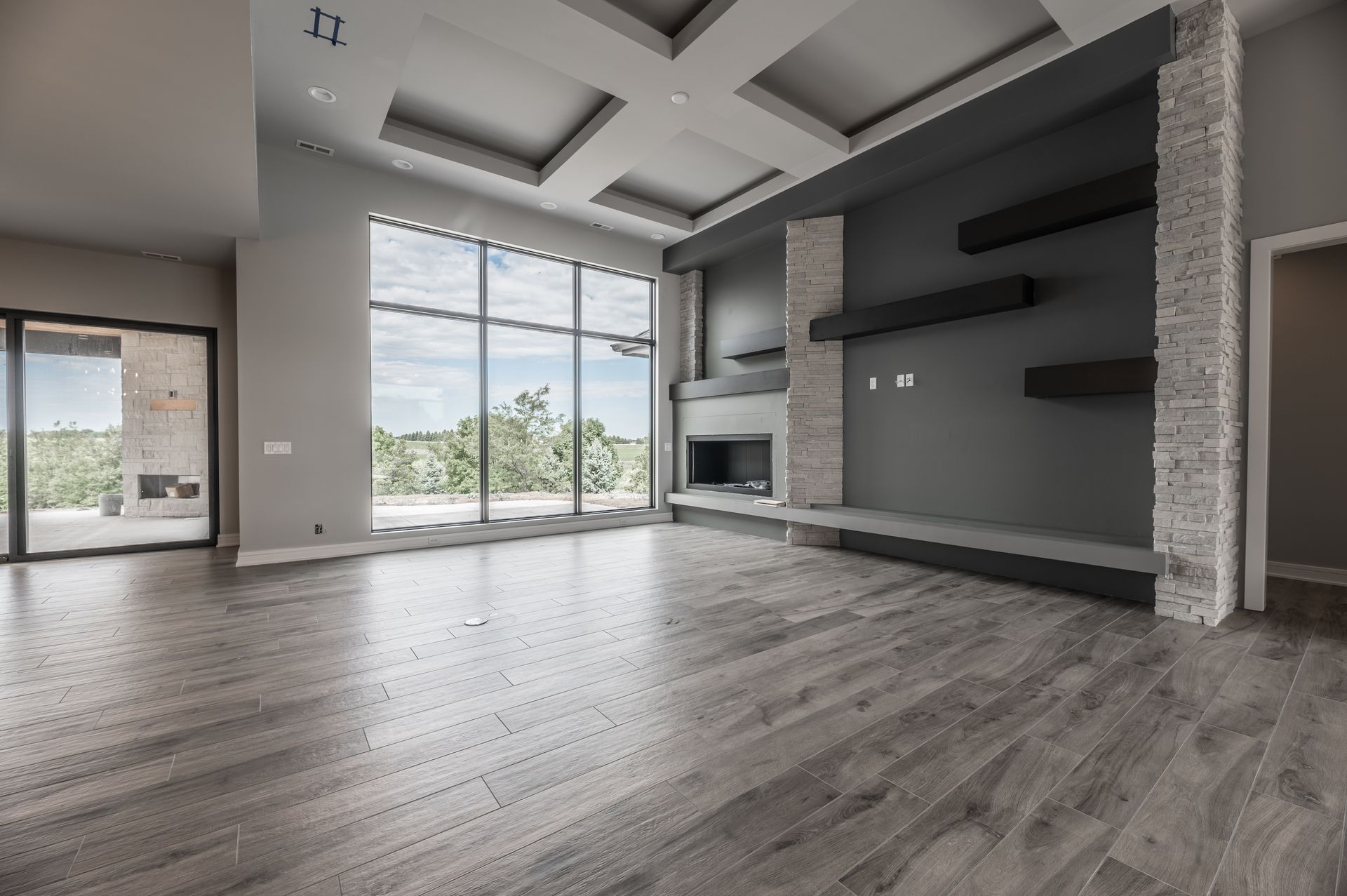 Empty modern living room with large windows and gray walls, fireplace.