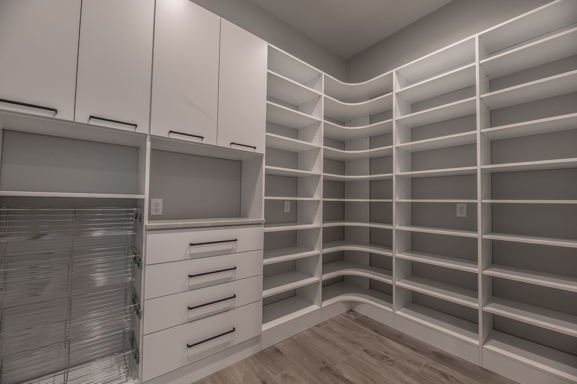 White walk-in closet with shelves and drawers. Hardwood floor. Cabinets on left side, shelving wraps around the corner.