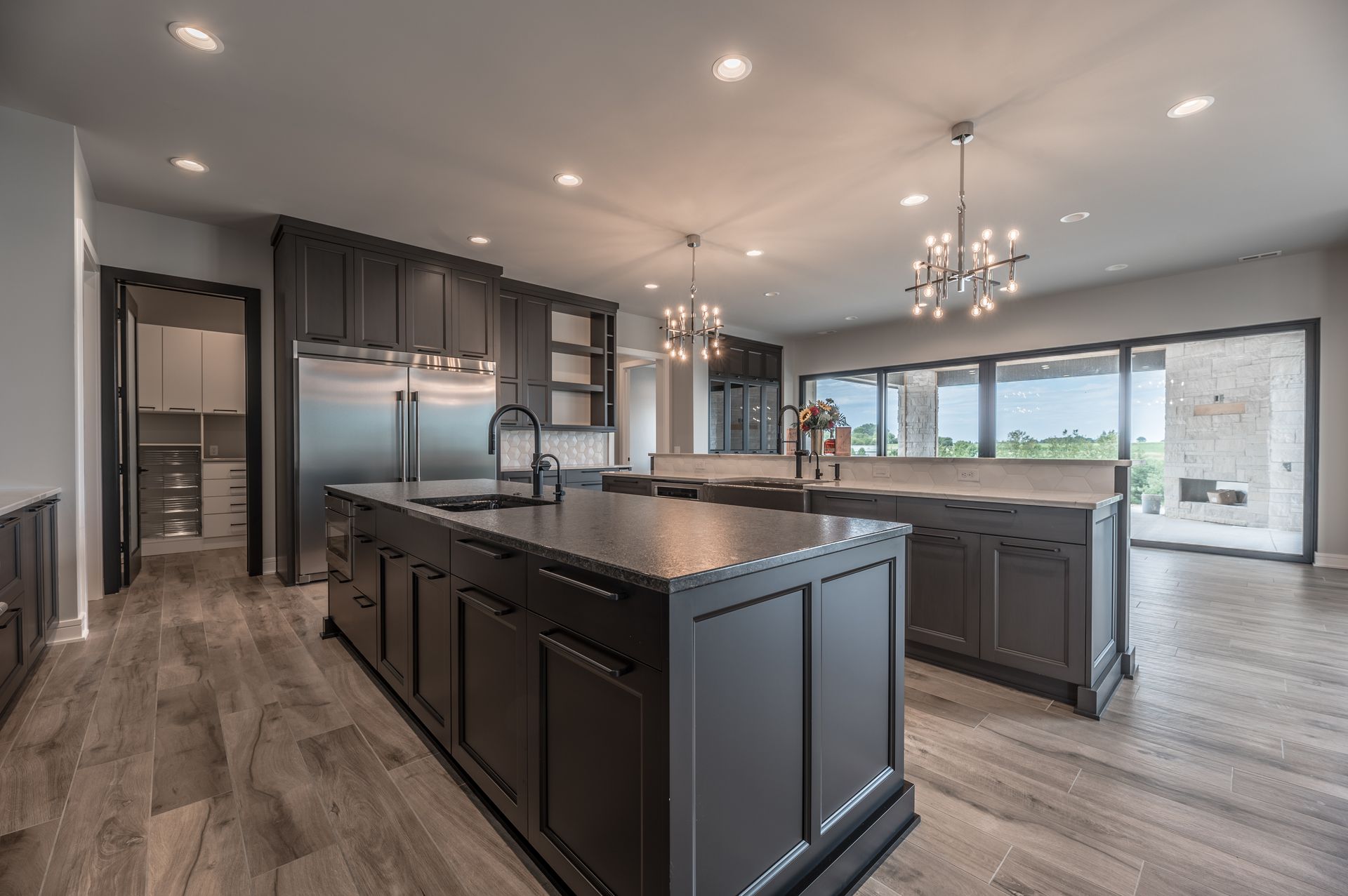 Modern kitchen with dark cabinetry, two islands, and large windows.