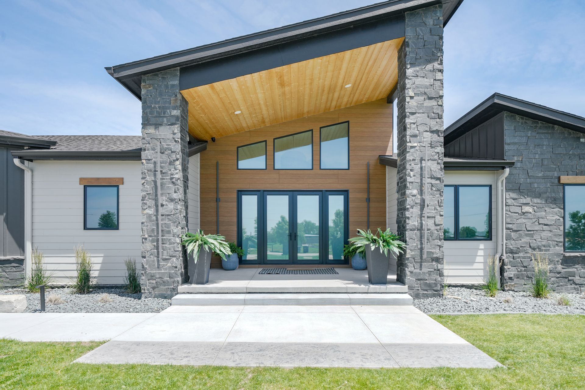 Modern house exterior with stone columns and wood accent, glass door entrance.