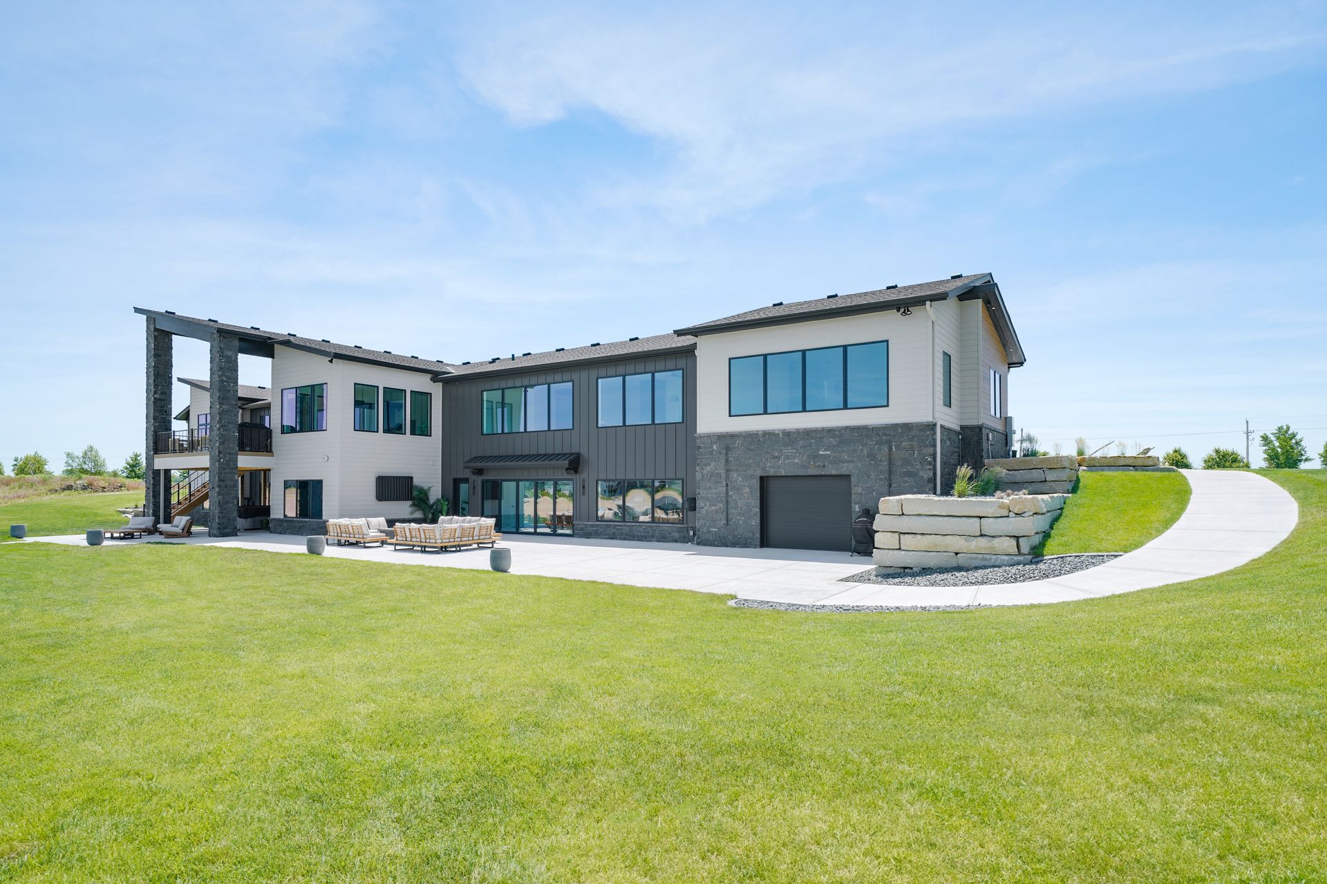 Modern two-story house with black and gray exterior, large windows, and a curved driveway on a sunny day.