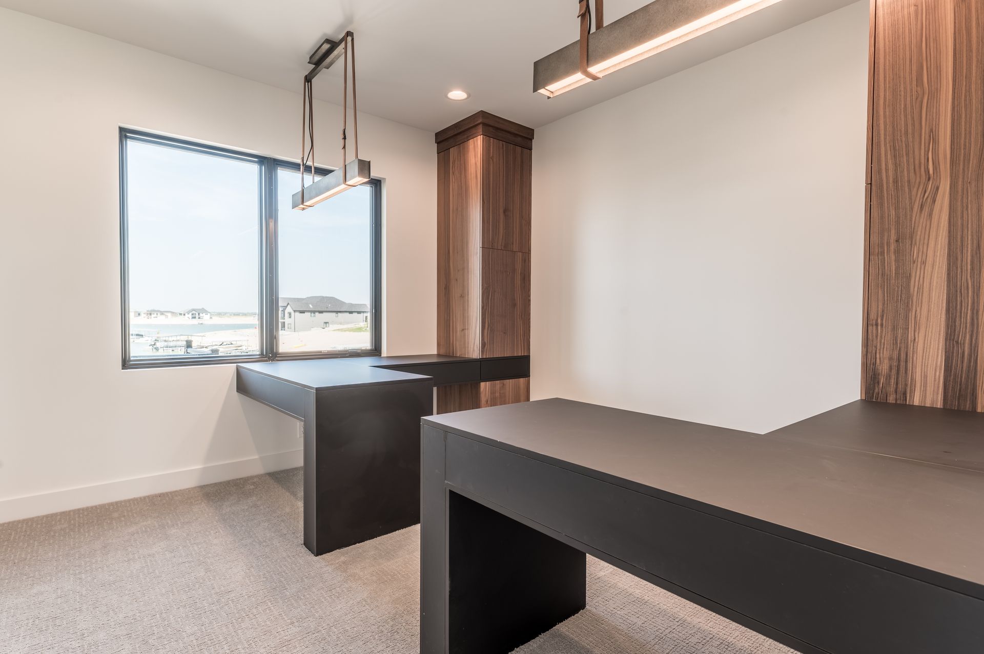 Modern office with two dark desks, a large window, and light-colored carpet.