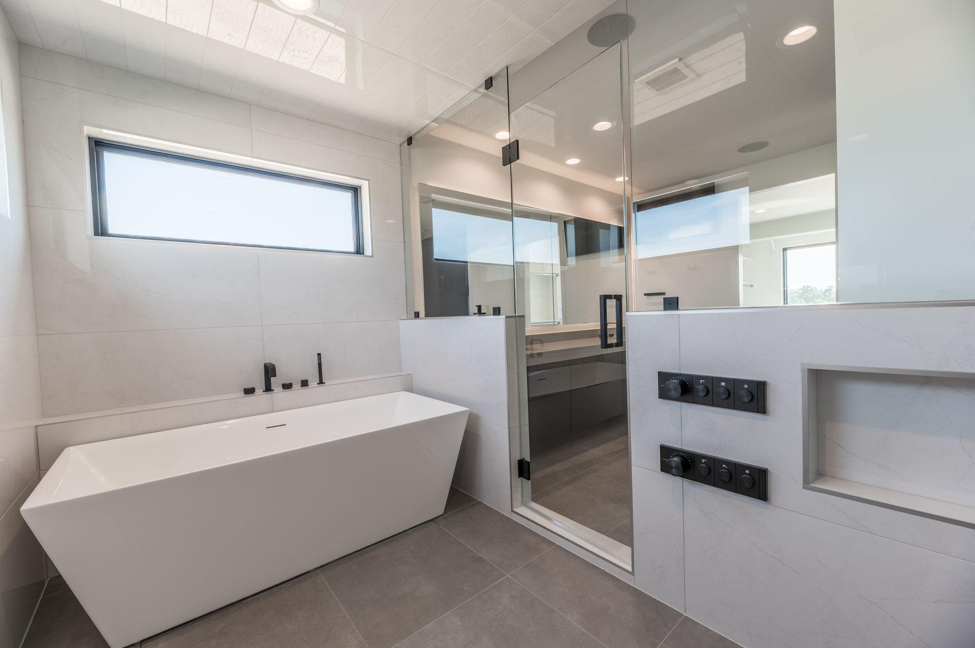 Modern white bathroom with a soaking tub, glass shower, and gray tile floor.