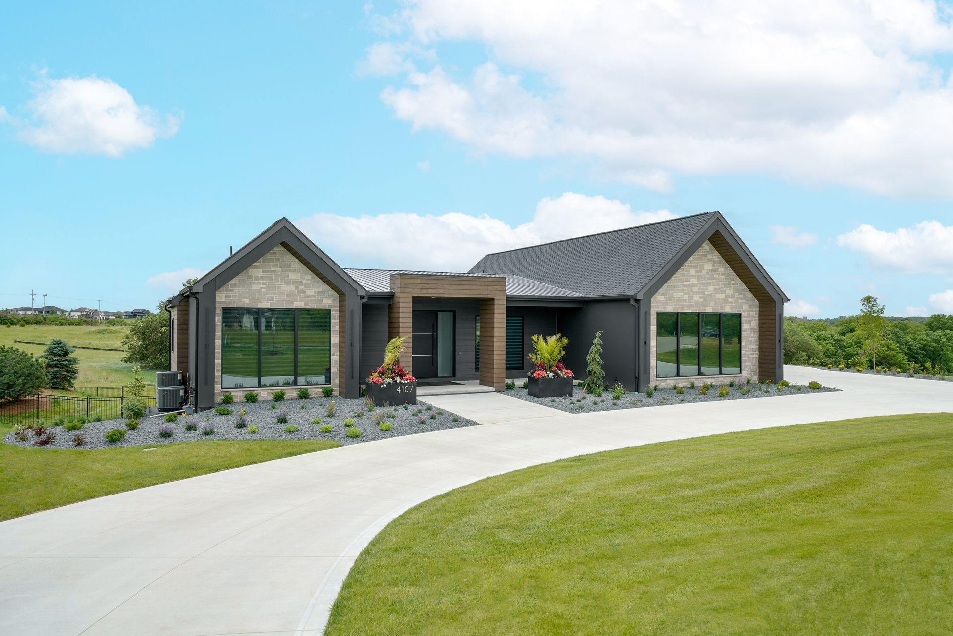 Modern house with dark siding, stone accents, large windows, and a long driveway.