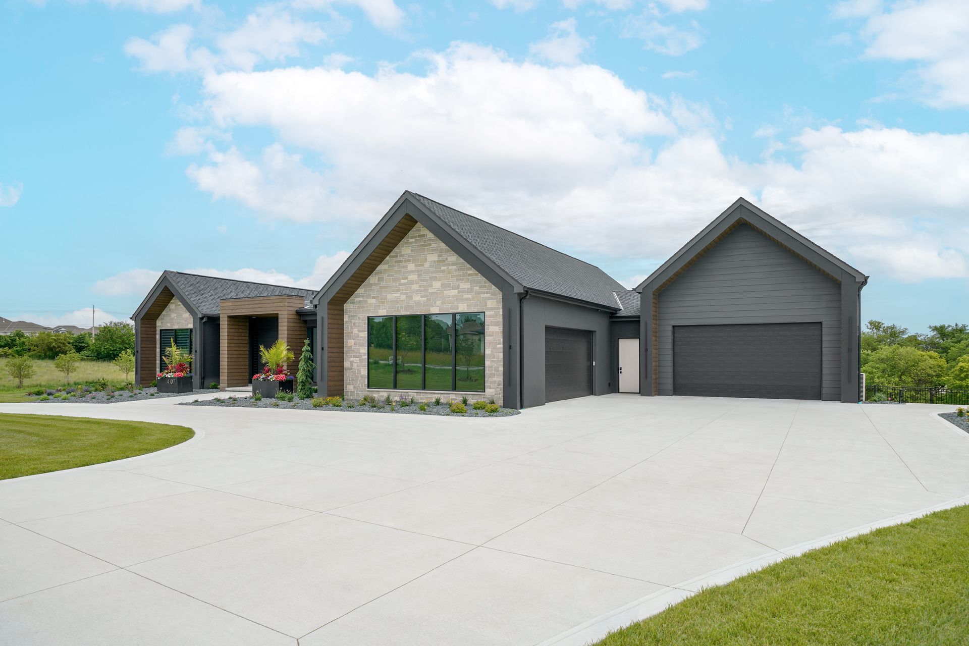Modern home with gray exterior, stone accents, and a wide concrete driveway under a blue sky.