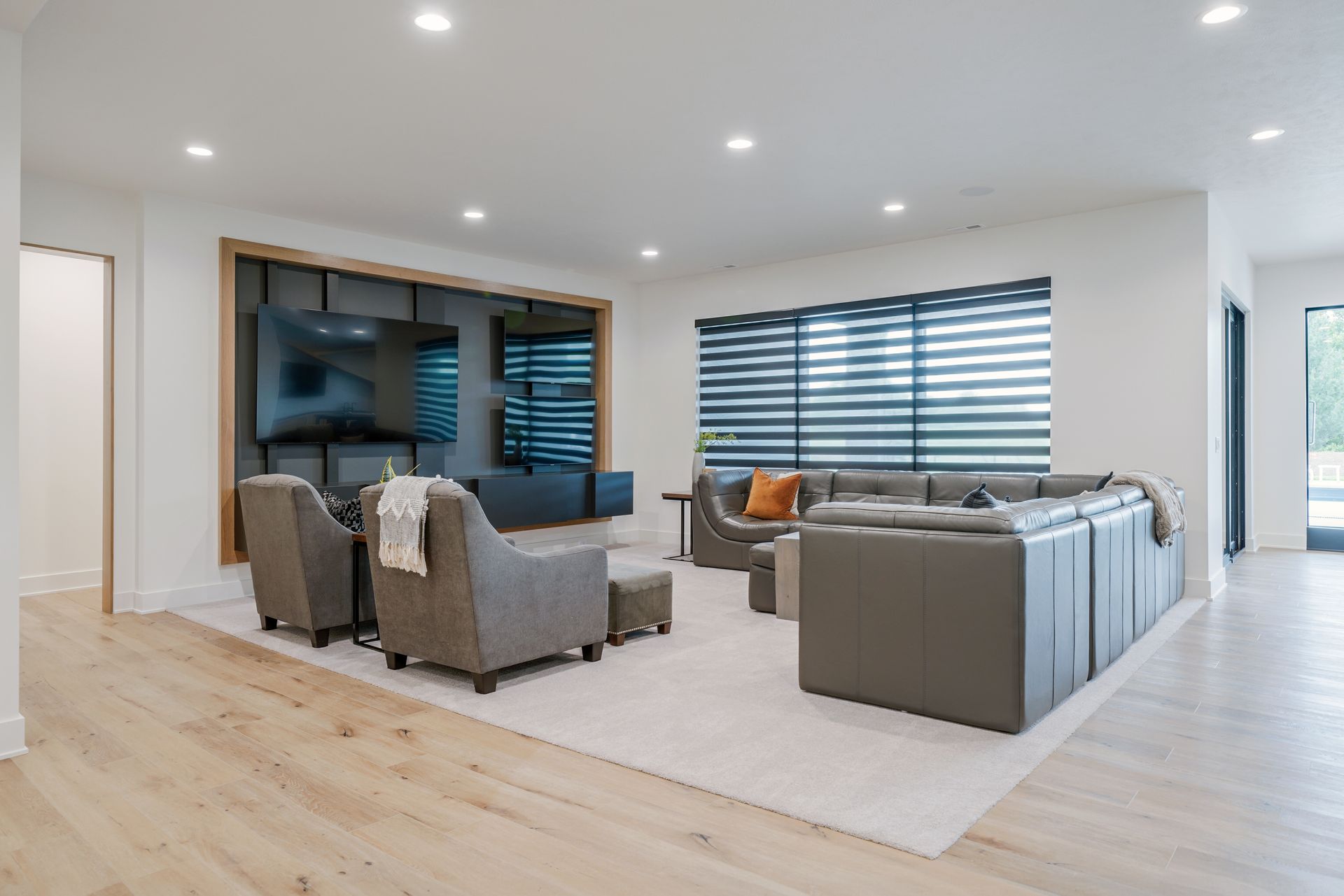 Modern living room with light wood floors, a gray sectional sofa, and armchairs.