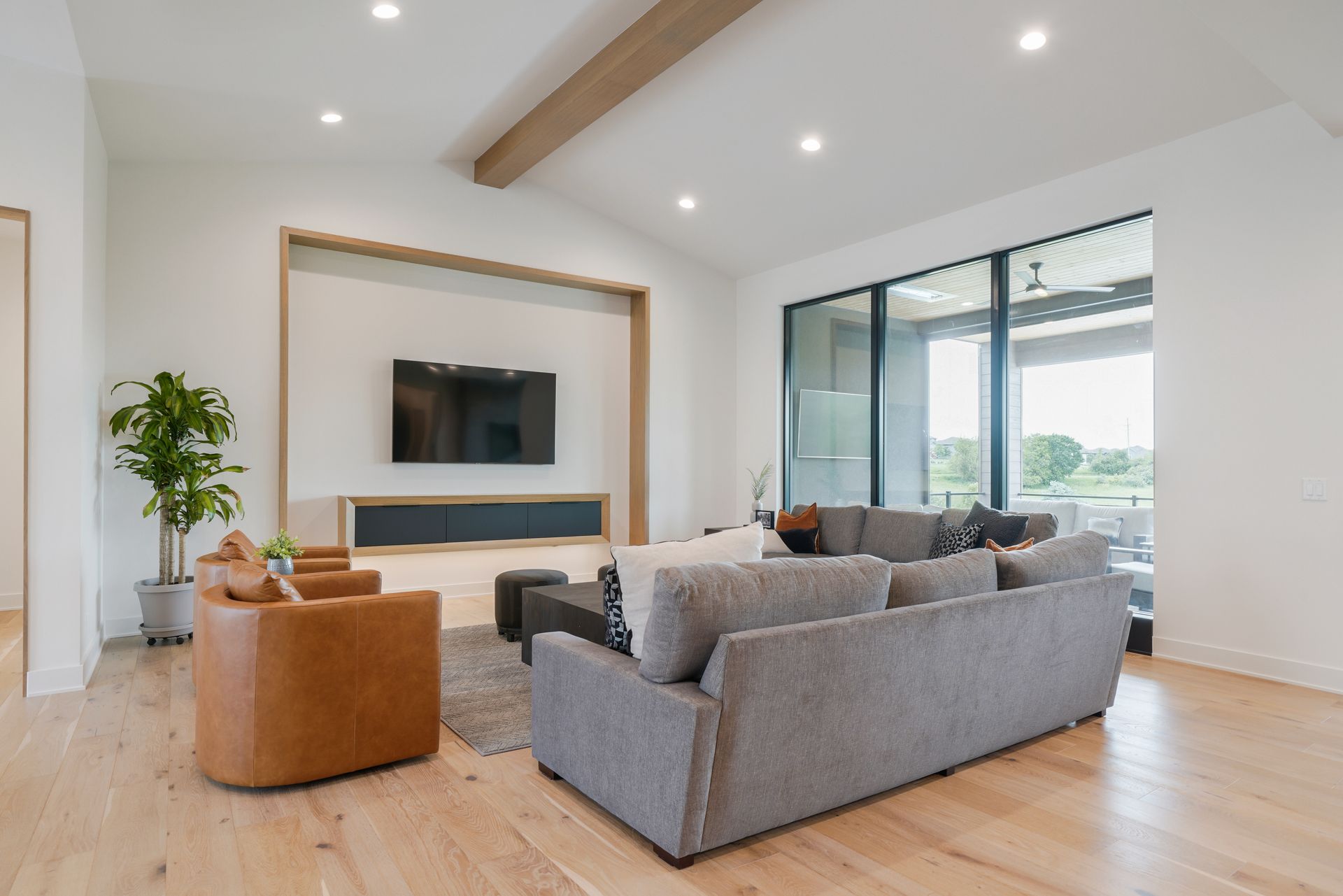 Modern living room with light wood floors, gray and brown couches, and large sliding glass doors.