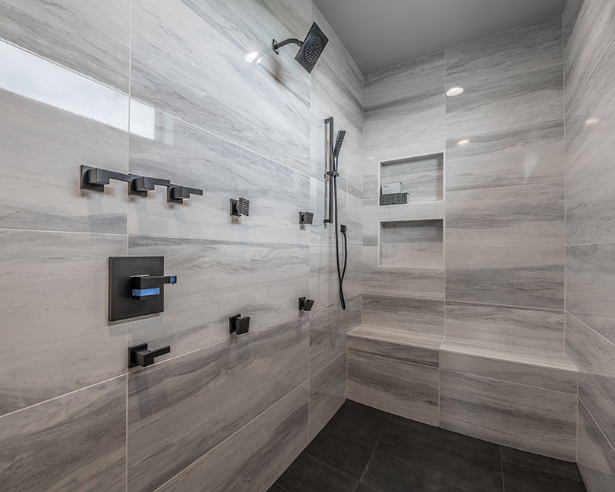 Modern bathroom shower with gray marble-look tile, black fixtures, built-in bench, and shower head.