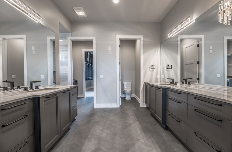 Spacious modern bathroom with gray cabinets, dual sinks, large mirrors, and a separate toilet room.