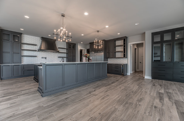 Spacious gray kitchen with a large island, cabinets, white backsplash, and two chandelier lights.