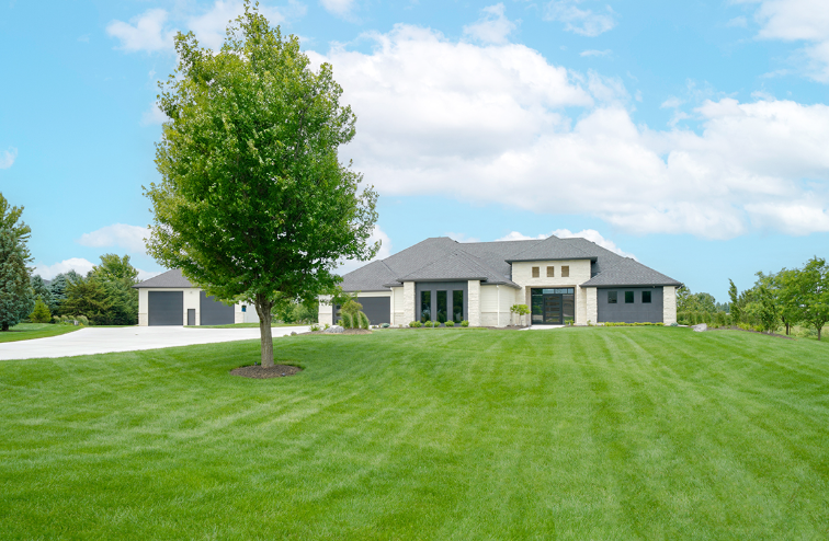 Sprawling house with stone and dark accents on manicured lawn under a blue sky.
