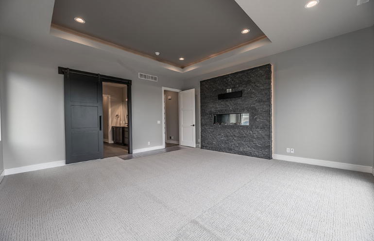 Empty bedroom with gray walls, carpet, and a fireplace. A sliding black door leads to a bathroom.
