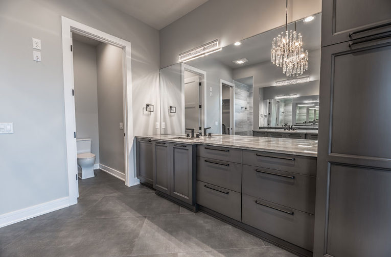 Gray bathroom with vanity, large mirror, and toilet in a separate room.