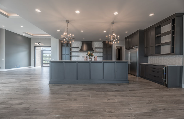 Modern gray kitchen with large island, stainless steel appliances, and two chandeliers.