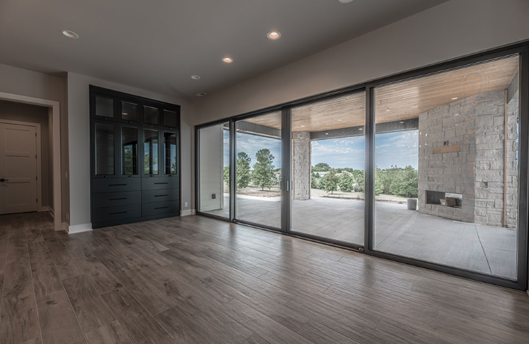Empty room with large sliding glass doors, dark cabinets, and wood flooring. Outside, a patio with a fireplace.