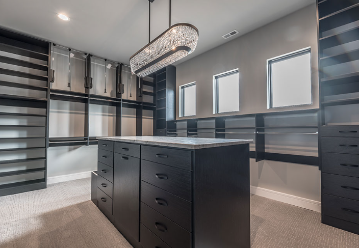 Walk-in closet with dark wood cabinetry, a central island, and a crystal chandelier.