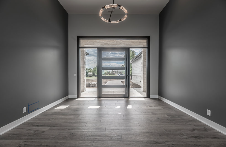 Gray entryway with dark gray walls, glass door, and wooden floor. A modern chandelier hangs from the ceiling.