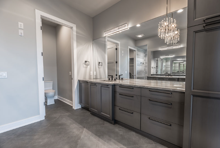 Gray bathroom with vanity, large mirror, and open doorway to a toilet.