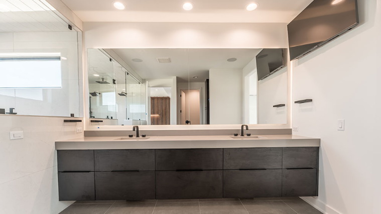 Modern bathroom with dark gray vanity, large mirror, and recessed lighting.