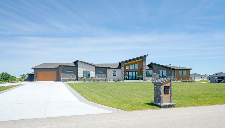 Modern home with angled roof, large windows, and a concrete driveway on a bright day.