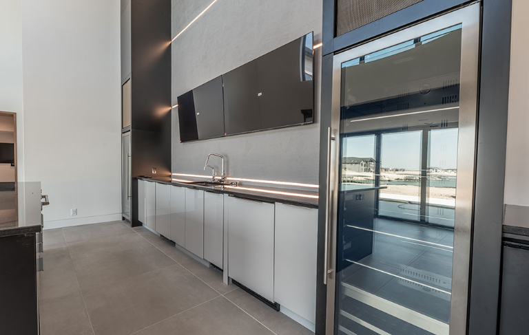 Modern kitchen area with white cabinets, a sink, and a black refrigerator. Large windows offer an outside view.