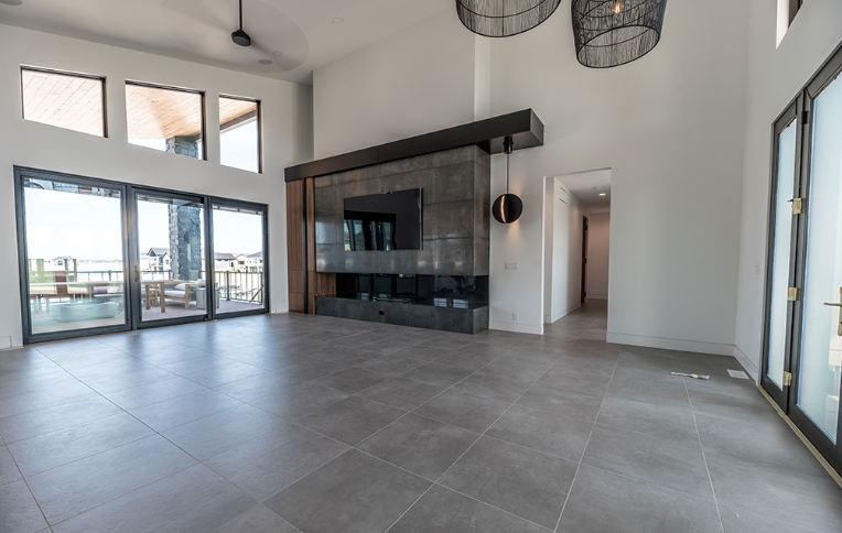 Empty, modern living room with large windows, fireplace, and gray tiled floor.