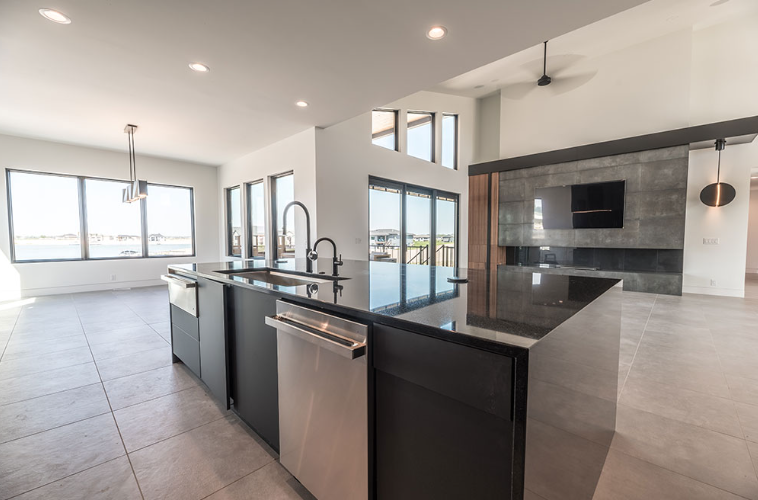 Modern kitchen with black island, stainless steel appliances, and large windows overlooking water.