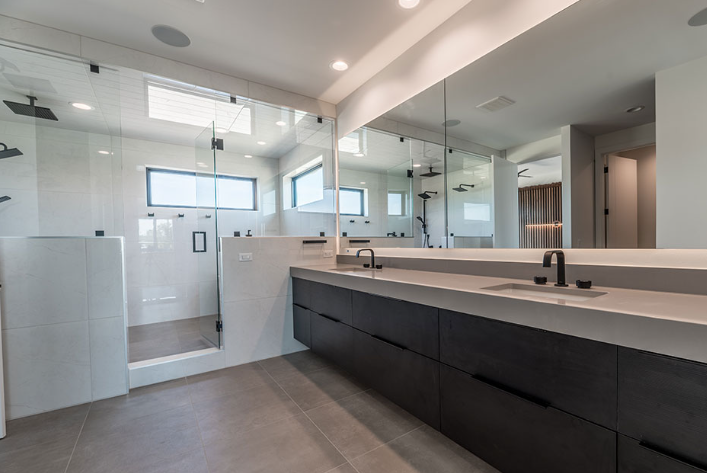 Modern bathroom with a glass-enclosed shower, dark cabinets, long mirror, and a gray countertop.
