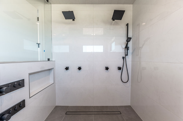 Modern white tile shower with two black shower heads, fixtures, and handheld shower.