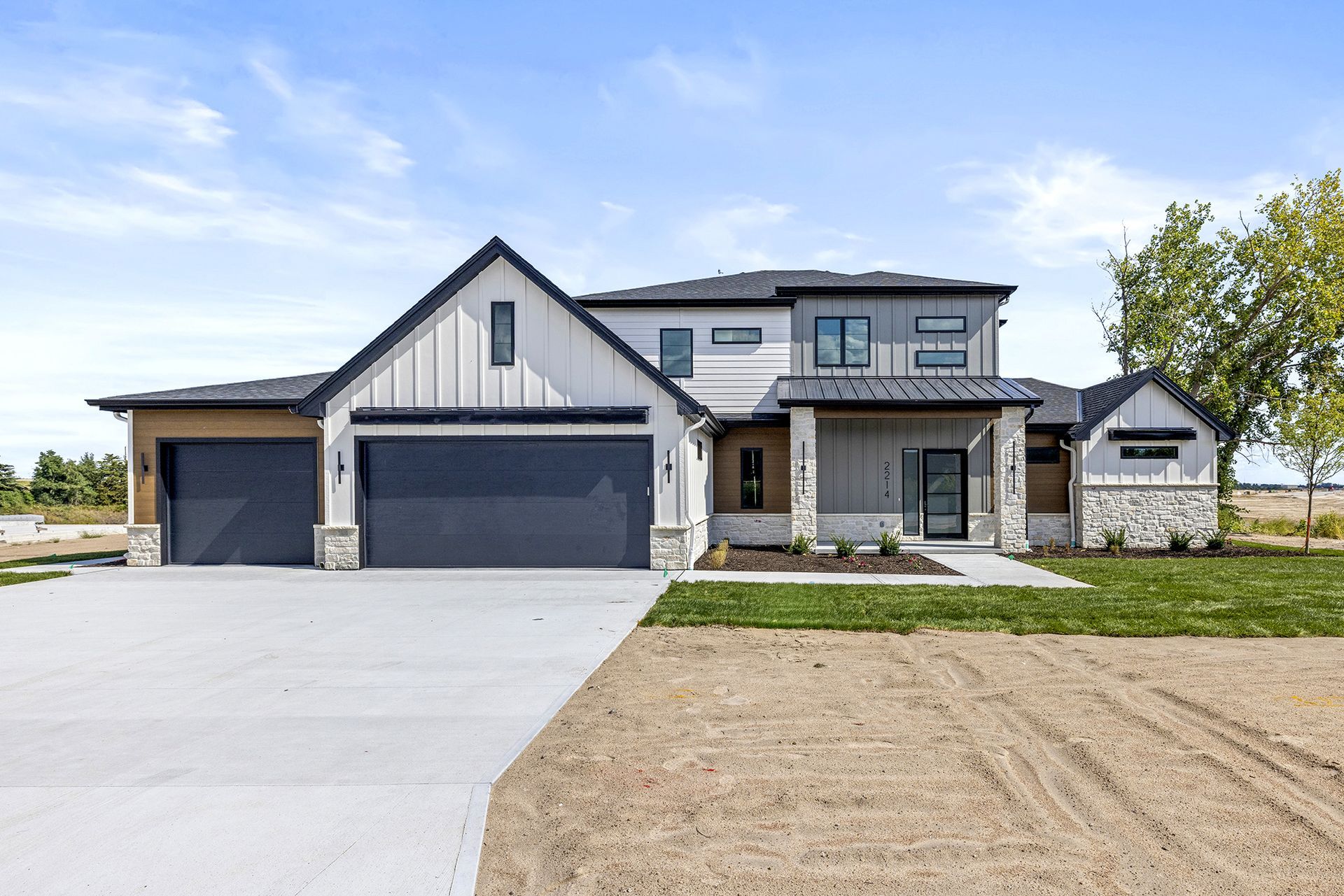 A modern two-story home with a white vertical siding, gray garage doors, and stone accents, set against a blue sky.