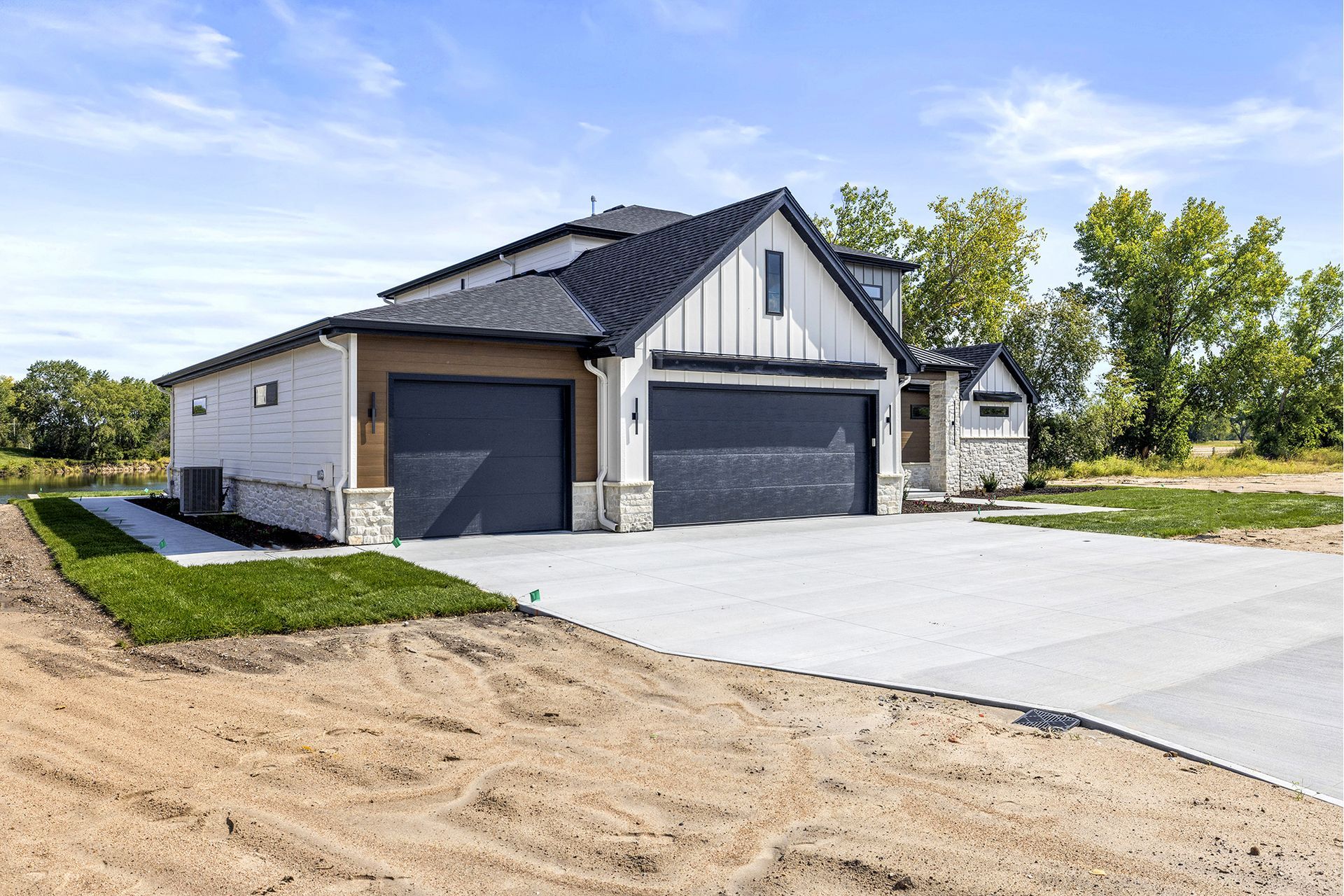A modern suburban home with a white exterior, dark gabled roof, and a three-car garage, set against a blue sky.