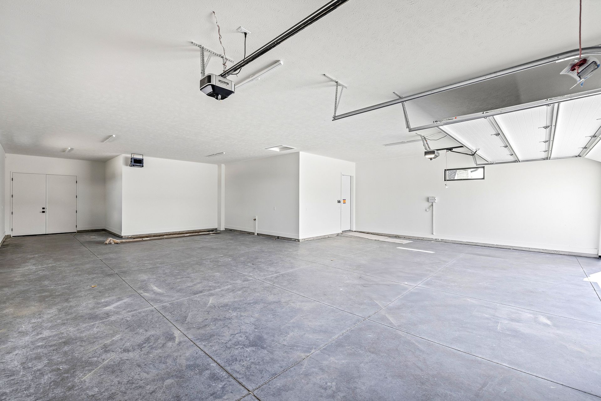 An empty, white-walled garage with a gray concrete floor and an open overhead garage door.