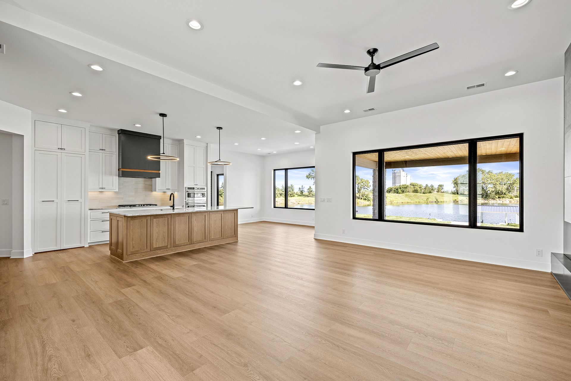 A modern open-plan living area and kitchen with light wood floors, white cabinets, a wood kitchen island, and a large view.