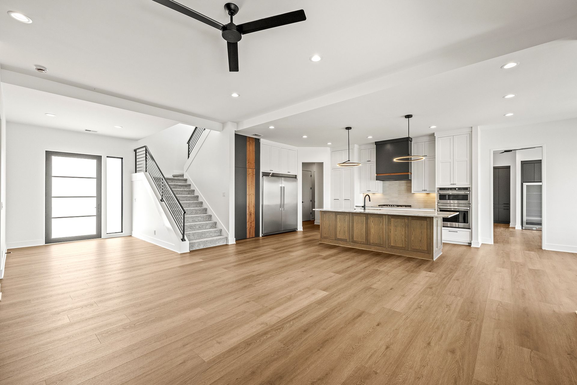 Open-plan home interior featuring light wood floors, a staircase with a black railing, and a modern kitchen with an island.