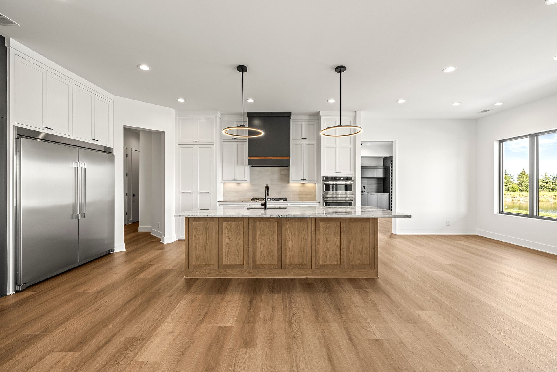 A spacious, modern kitchen featuring a large wooden island, white cabinetry, a stainless refrigerator, and wood floors.
