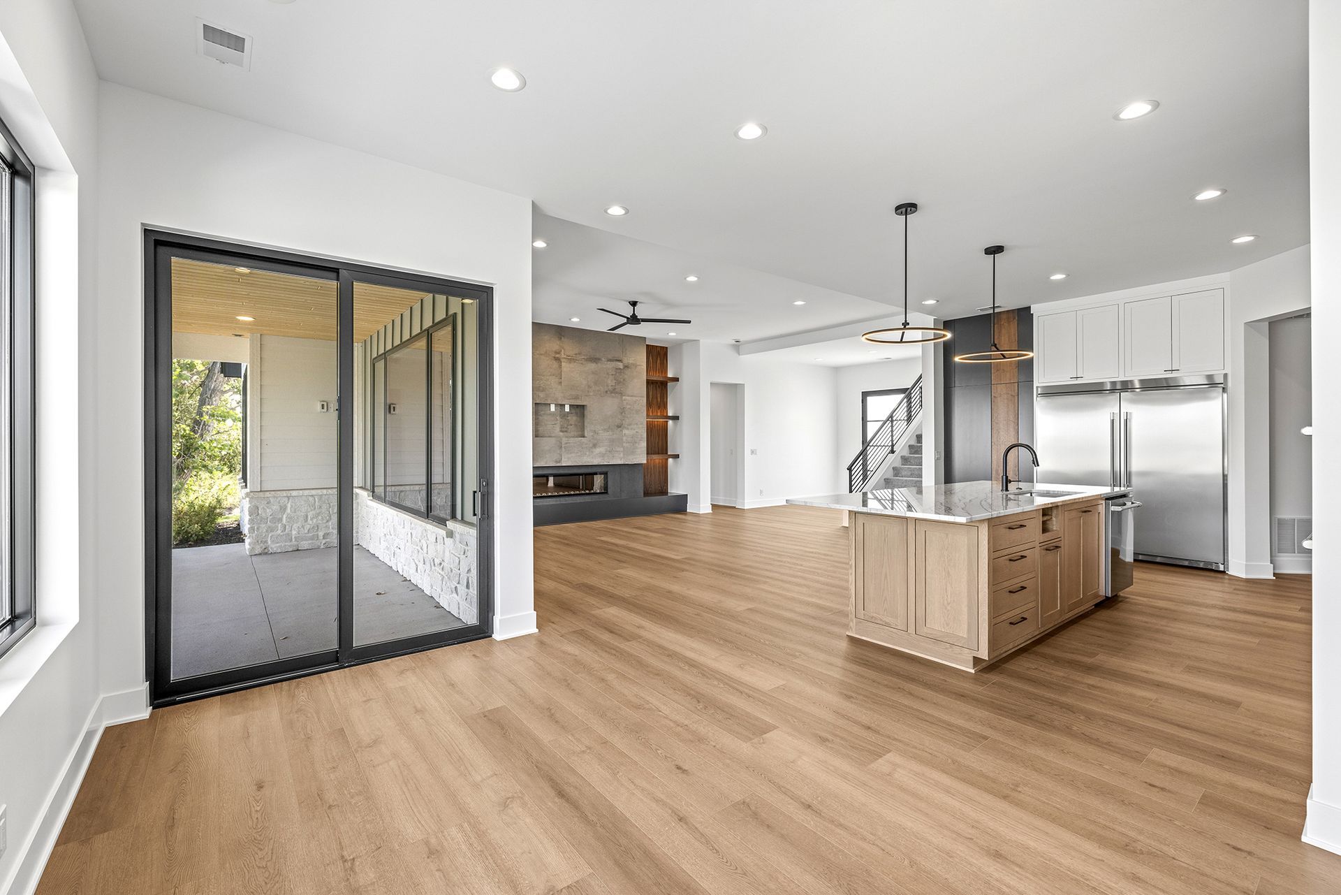 A modern open-concept home featuring light wood floors, a kitchen island, stainless appliances, and glass sliding doors.