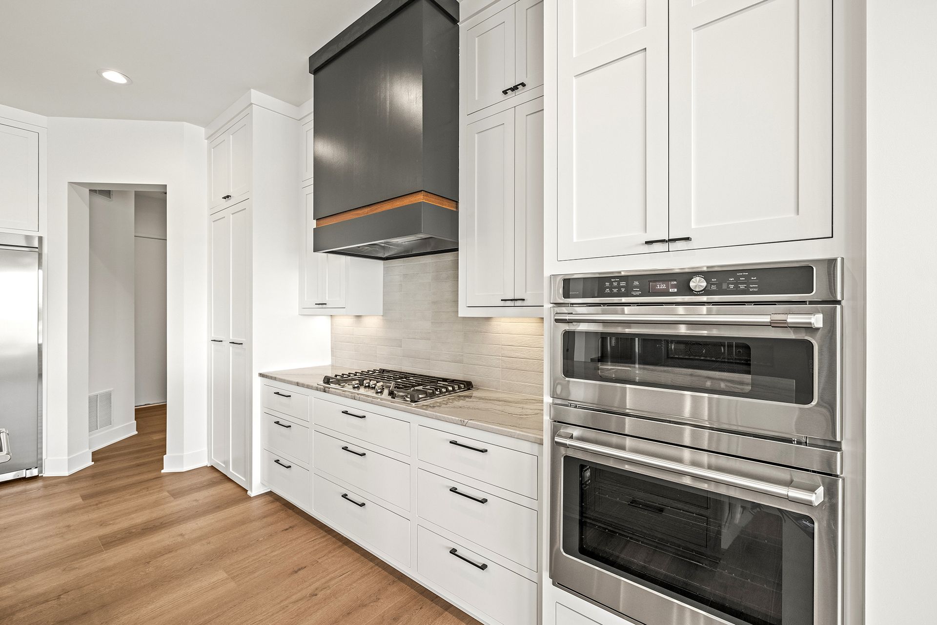 Modern kitchen featuring white cabinets, a charcoal range hood, stainless steel appliances, and wood floors.
