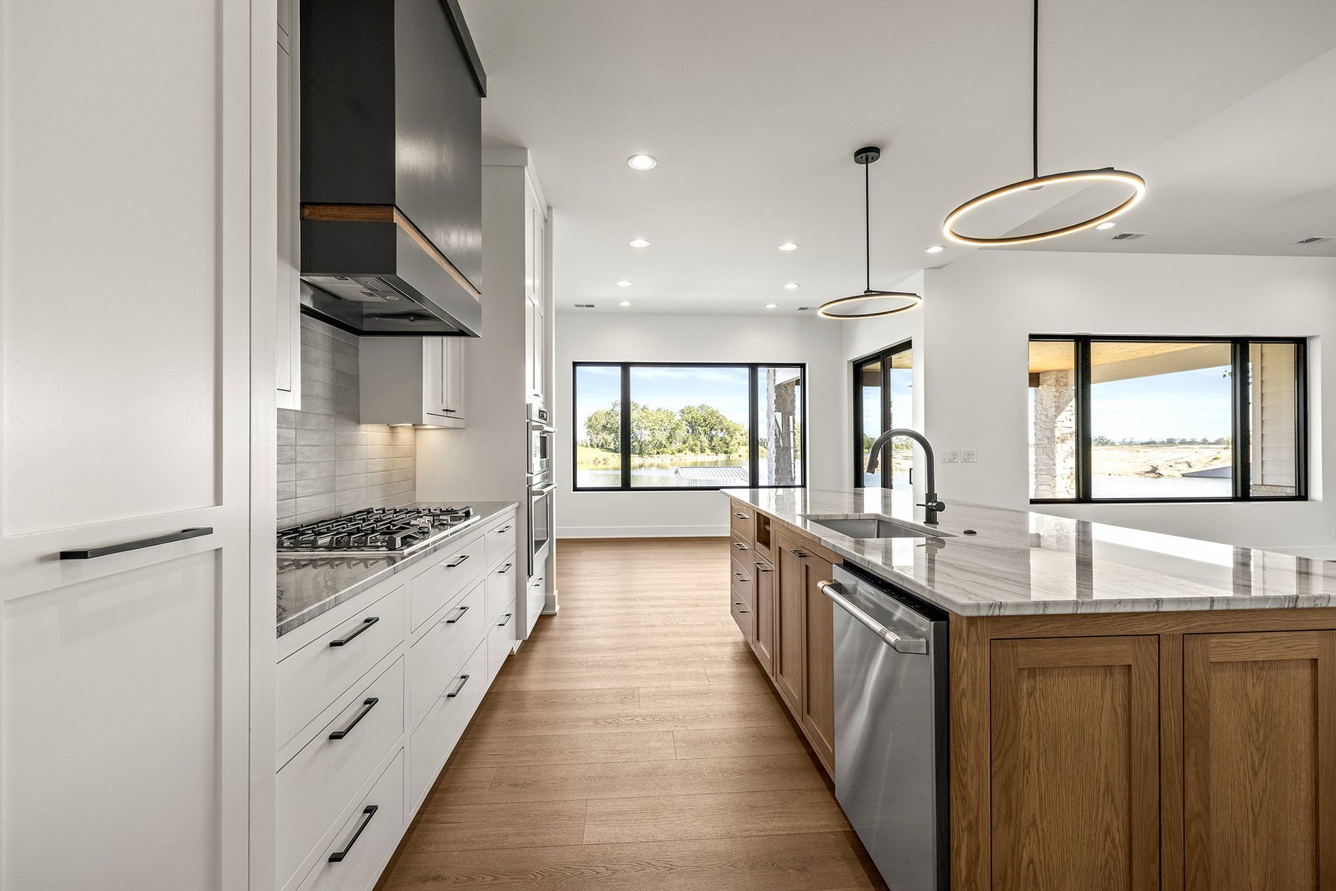 A modern kitchen featuring white cabinets, a wood-toned island, stainless steel appliances, and large windows.