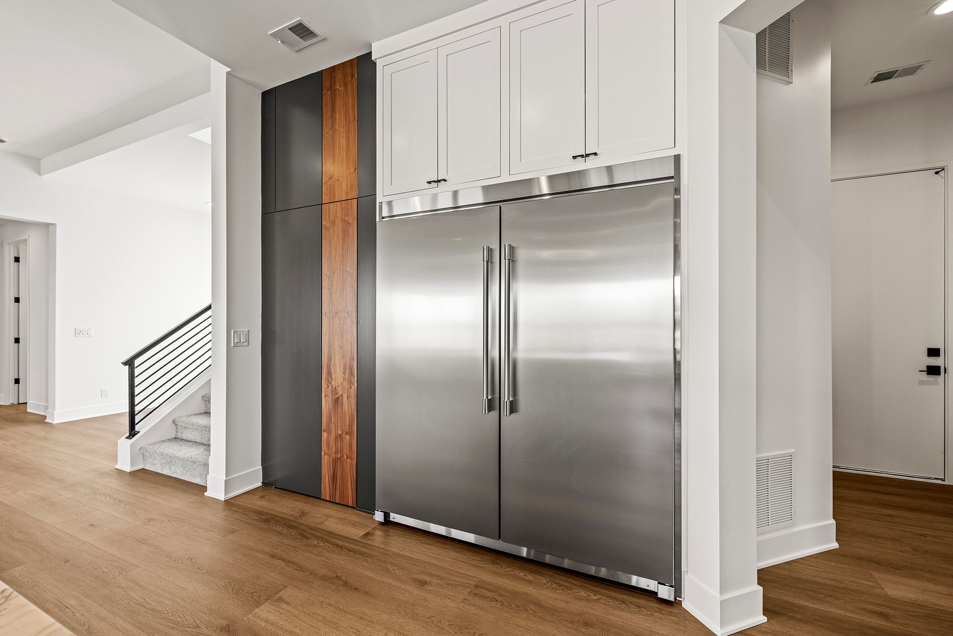 A stainless steel side-by-side refrigerator built into a wall with white cabinets and wood accents in a modern home.