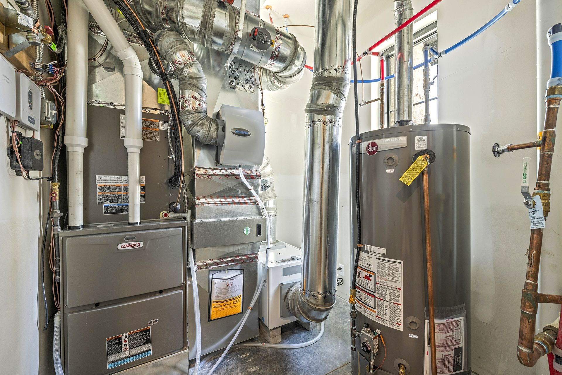 Utility closet containing a furnace, water heater, HVAC ductwork, and various plumbing pipes against a white wall.