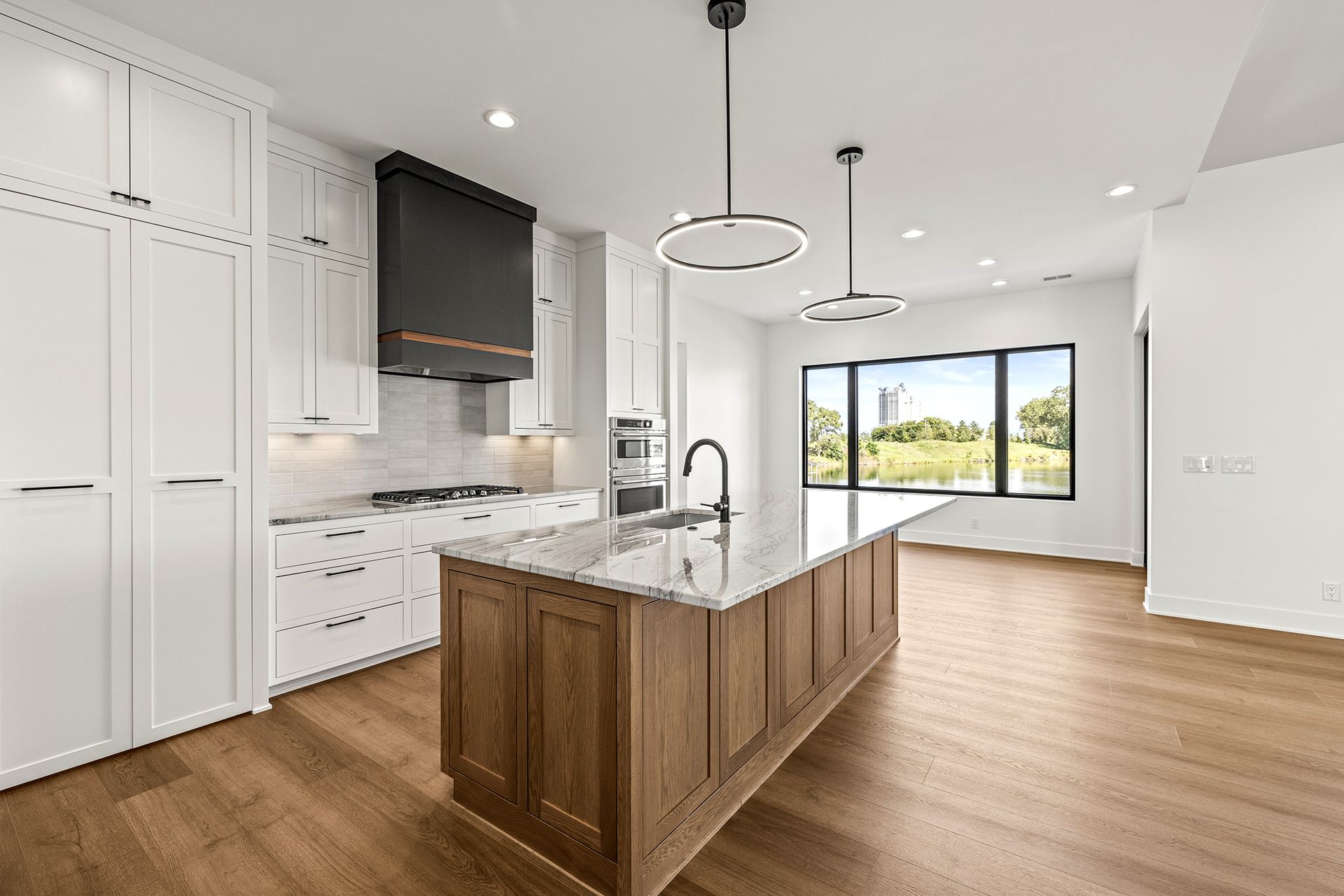 A modern kitchen features white cabinetry, a black range hood, a stained wood island with granite, and hardwood floors.