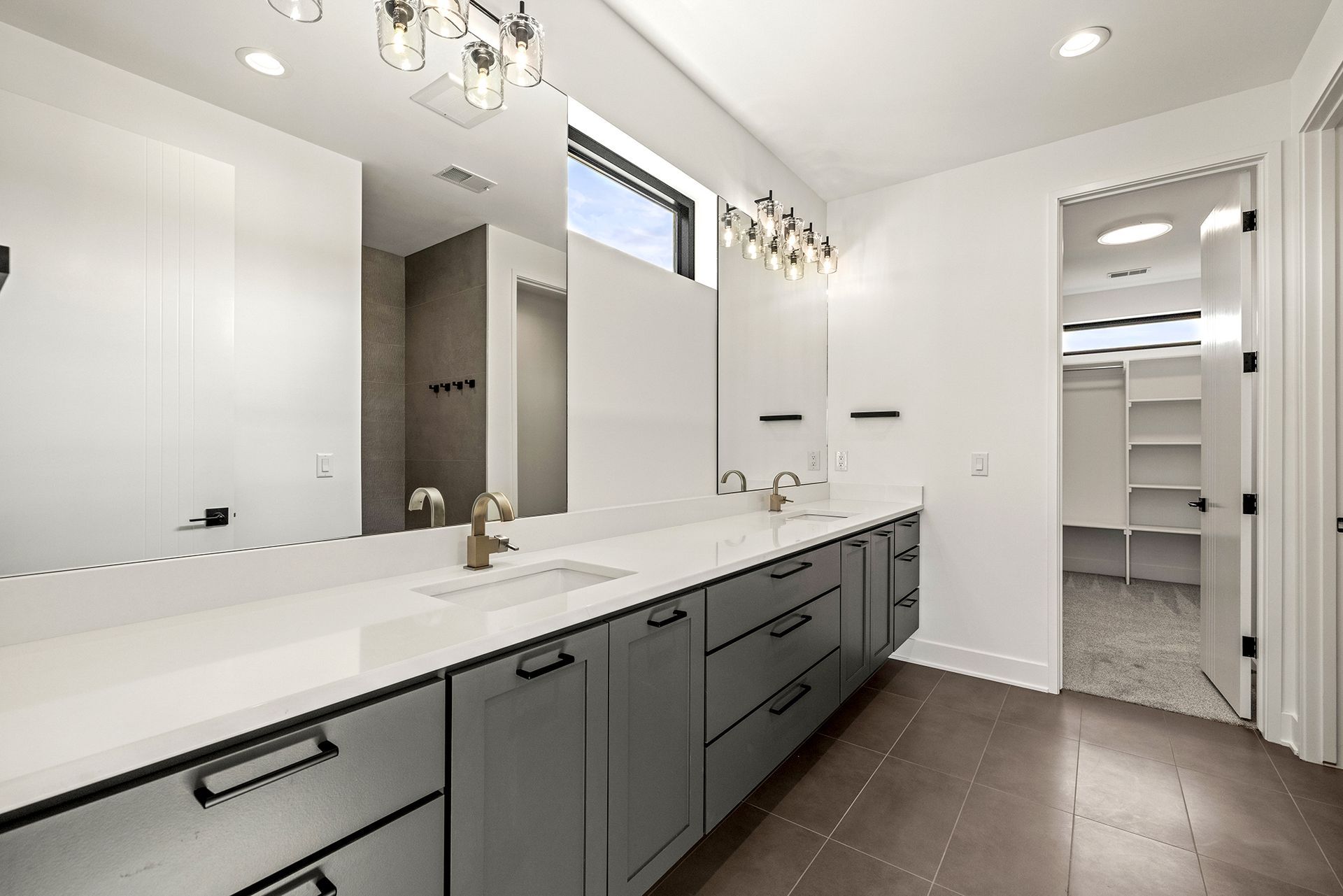 Modern bathroom vanity with dark gray cabinets, a white countertop, large wall-to-wall mirror, and open door to closet.