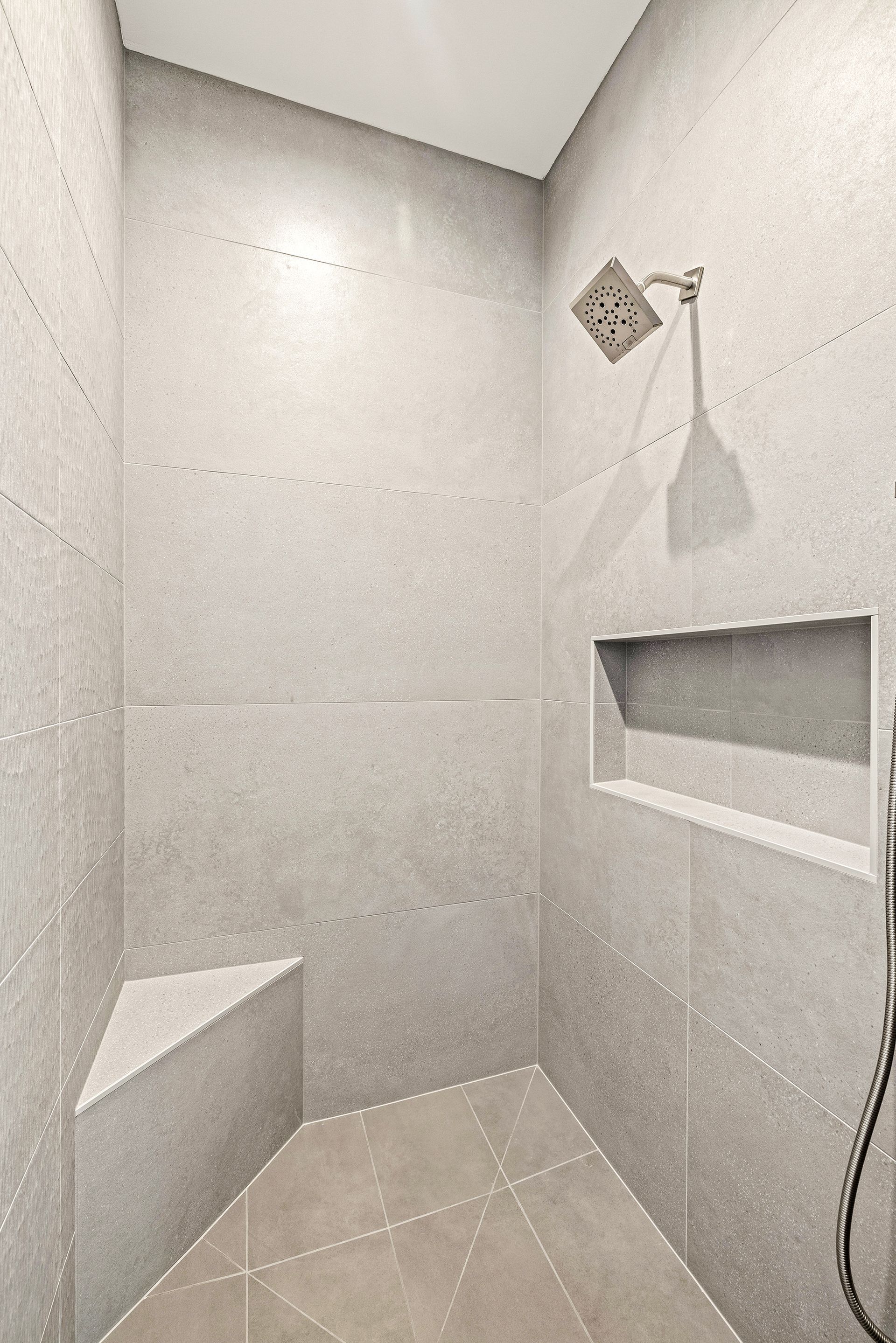 A walk-in shower with gray speckled tile walls, a built-in corner bench, a wall niche for toiletries, and a shower head.