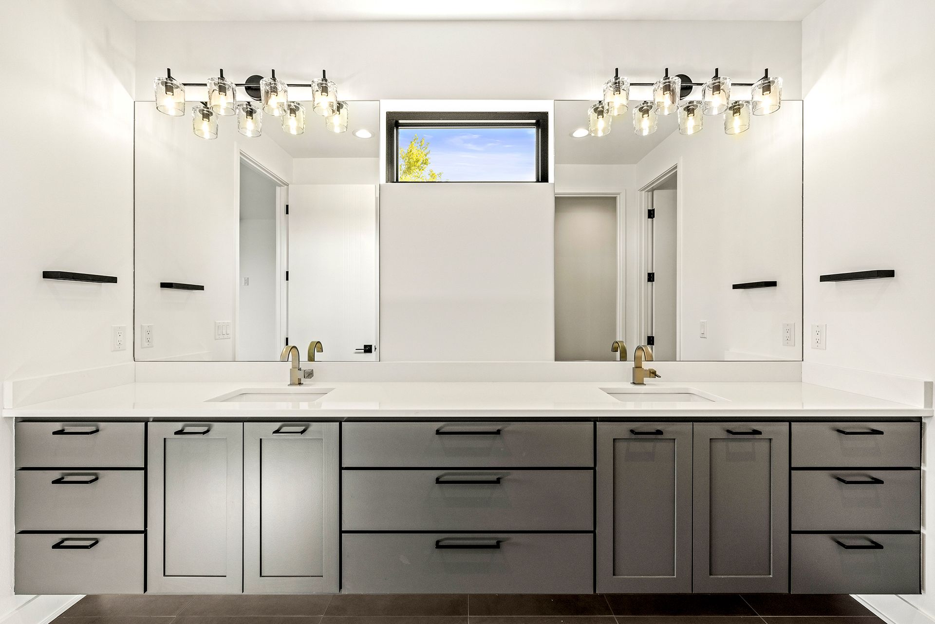 A double vanity bathroom with dark grey cabinets, white countertops, two sinks, mirrors, and modern lighting.