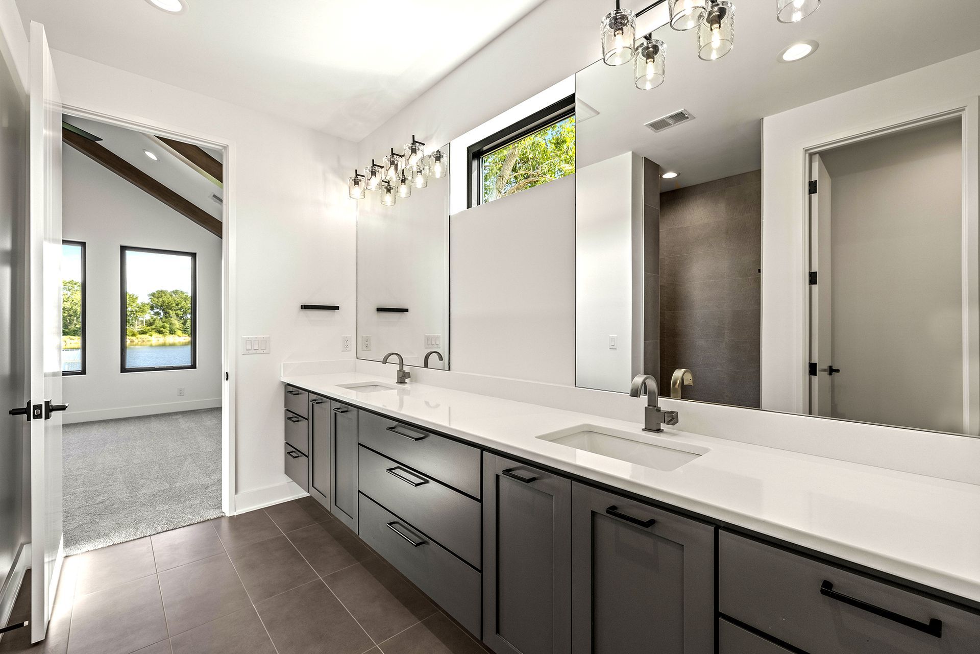 Modern bathroom featuring a double vanity with grey cabinets, white countertops, two mirrors, and dark tile flooring.