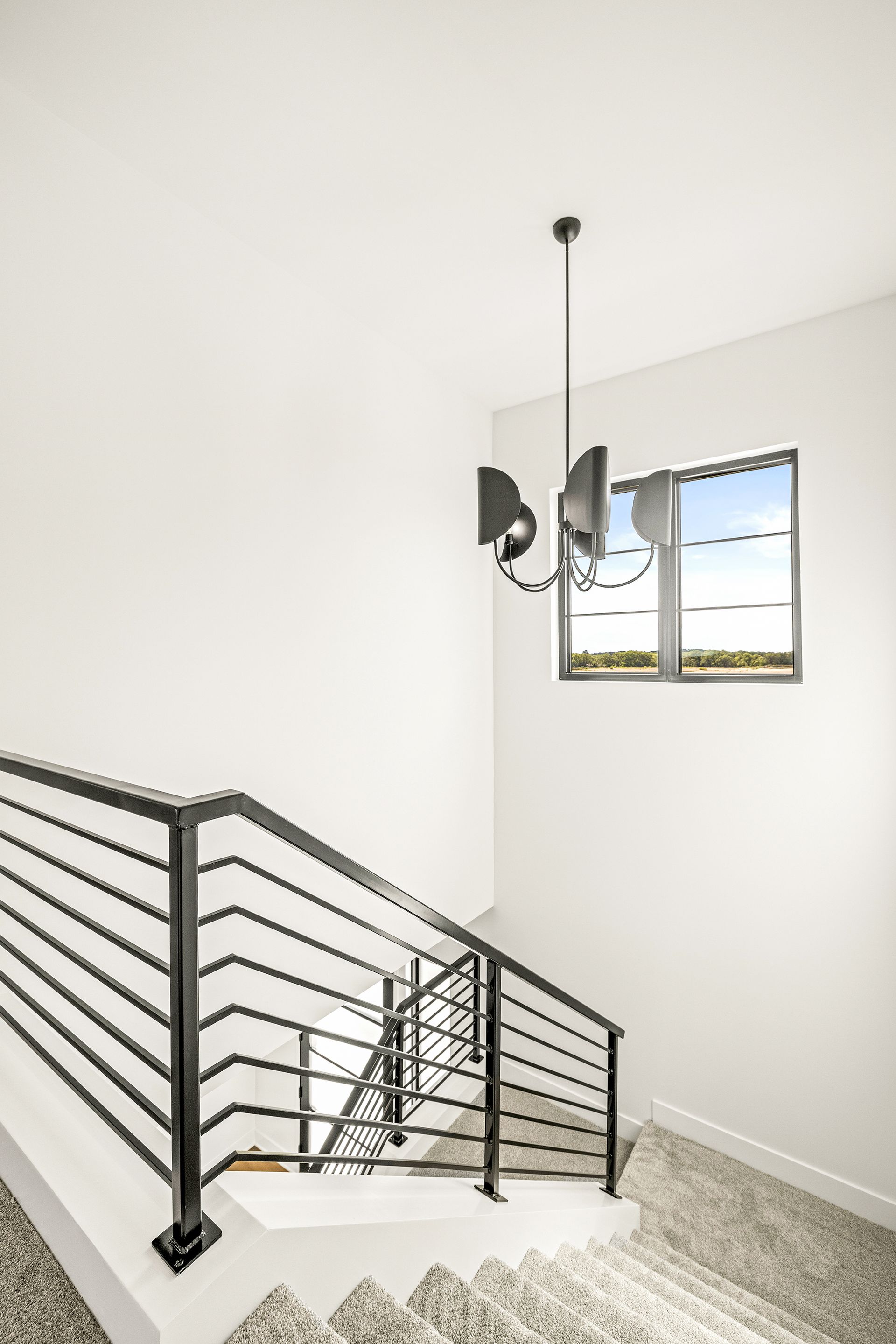 Modern staircase with a black metal horizontal railing, carpeted steps, and a pendant light next to a window.